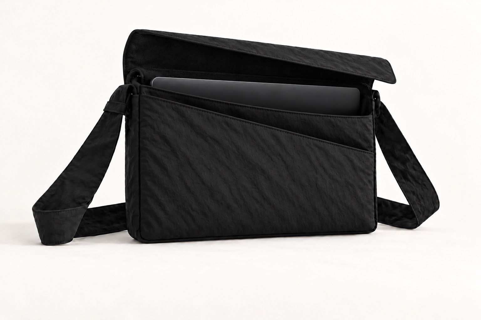 Open laptop carry concept showing a laptop in the main sleeve and a separate broad front accessory pouch with a diagonal opening covered by the top flap when closed.